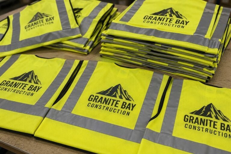 Custom hi-vis vests with company logo stacked in a site office